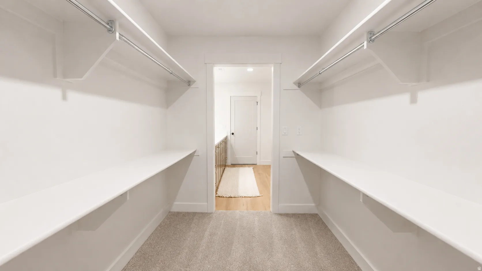Walk-in closet with light-colored carpeting, white shelving, and hanging rods