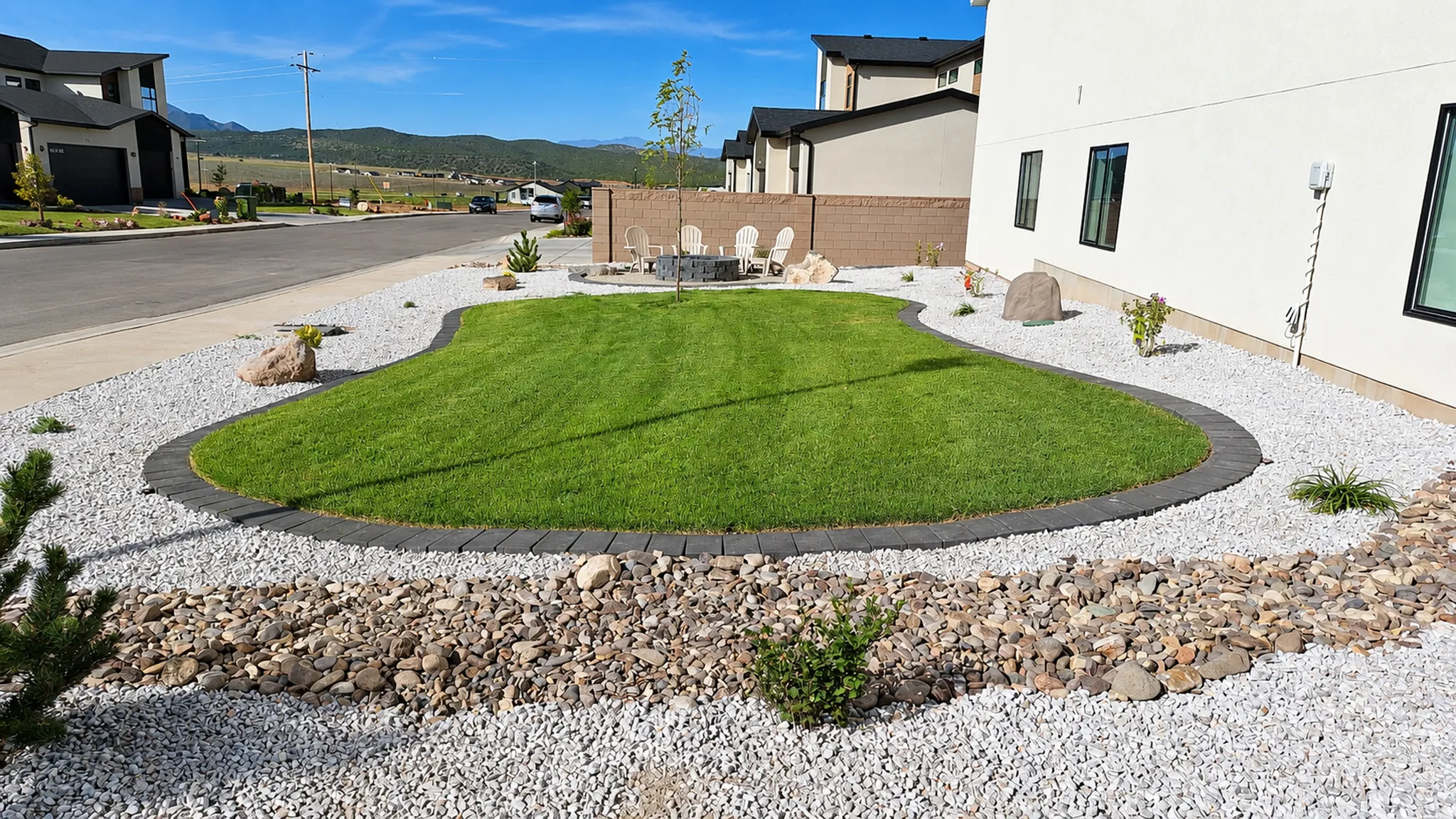 Manicured lawn with paver edging, surrounded by decorative white gravel, and a rock-lined dry creek bed