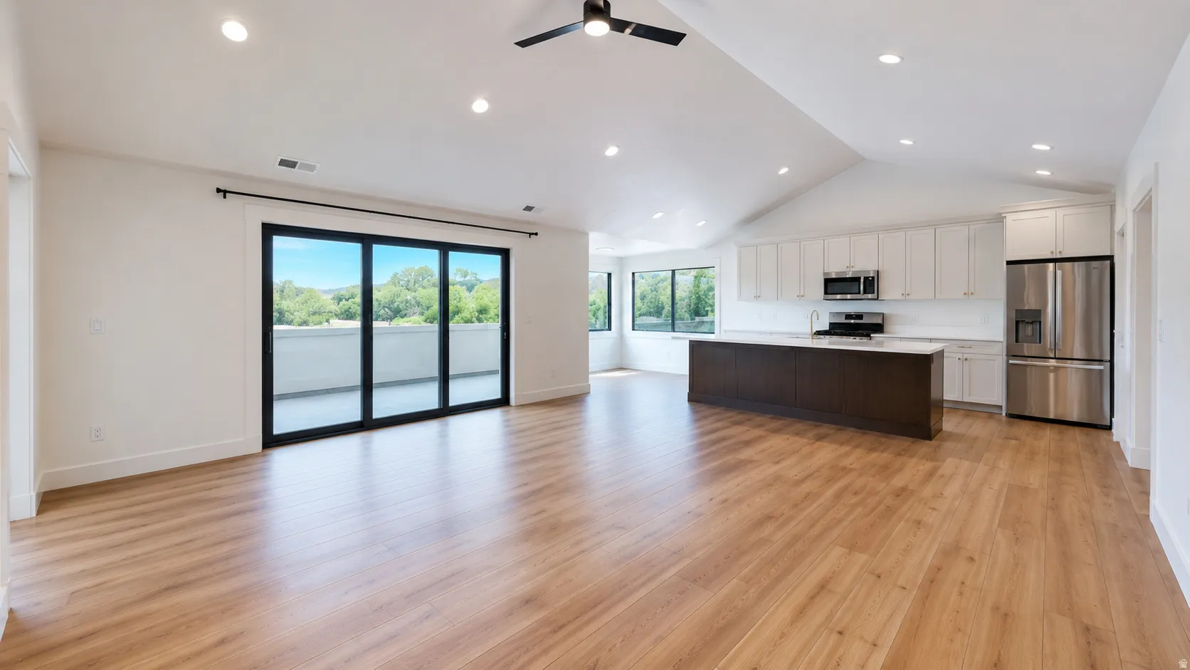Vaulted ceiling, recessed lighting, wood-finish flooring, sliding glass doors to a balcony, and a kitchen with stainless steel appliances