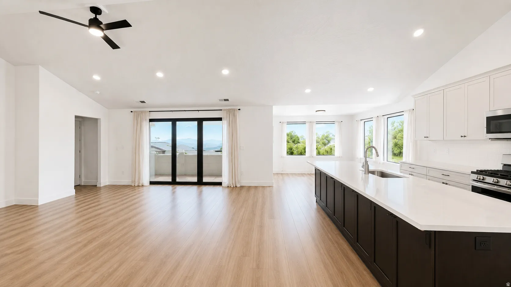 Vaulted ceilings with recessed lighting, wood-finish flooring, full kitchen with white cabinetry and dark island, stainless steel appliances, and glass doors to a balcony