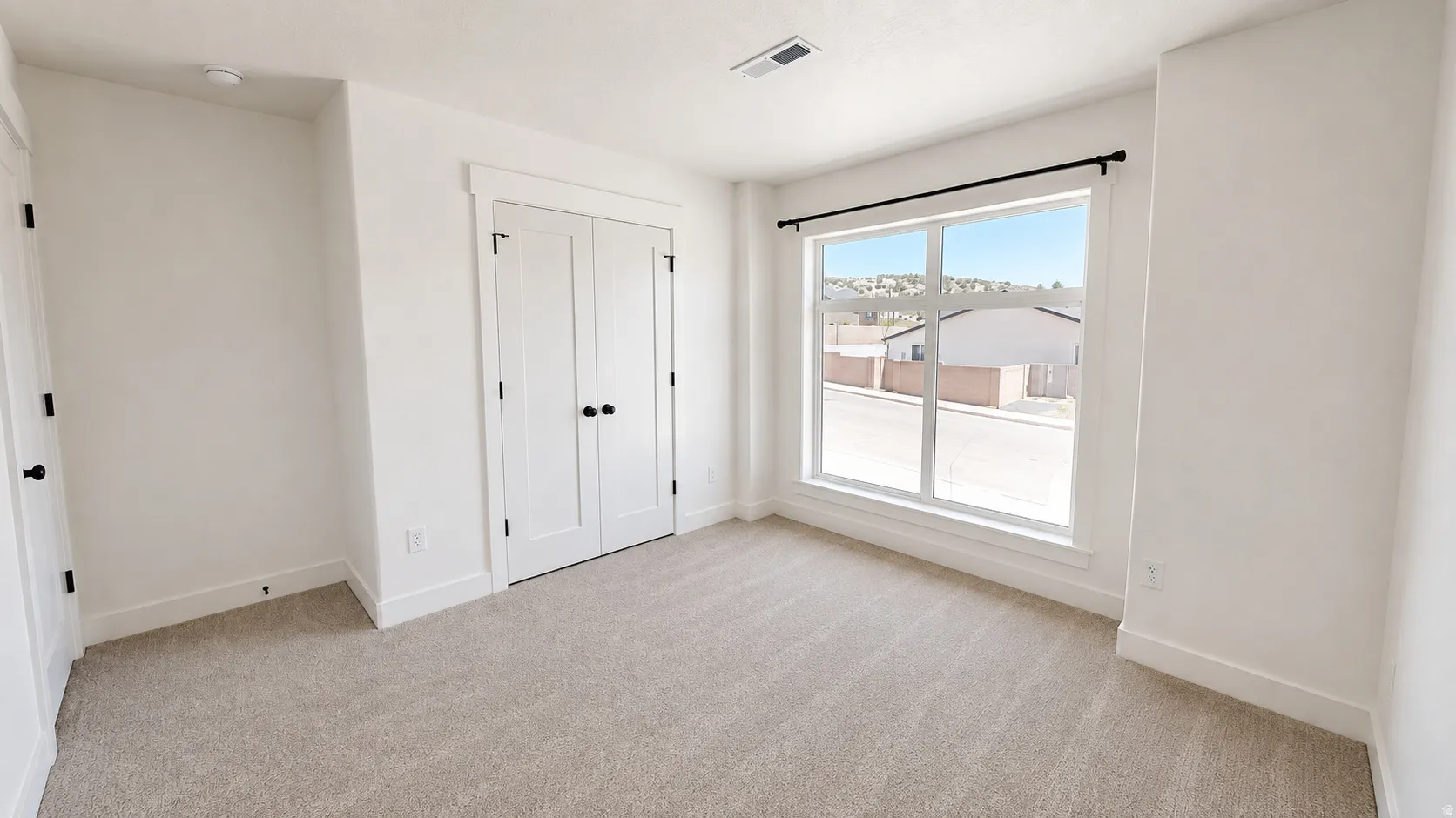 Neutral-toned carpeting, white walls, and a large window with black-finish curtain rod