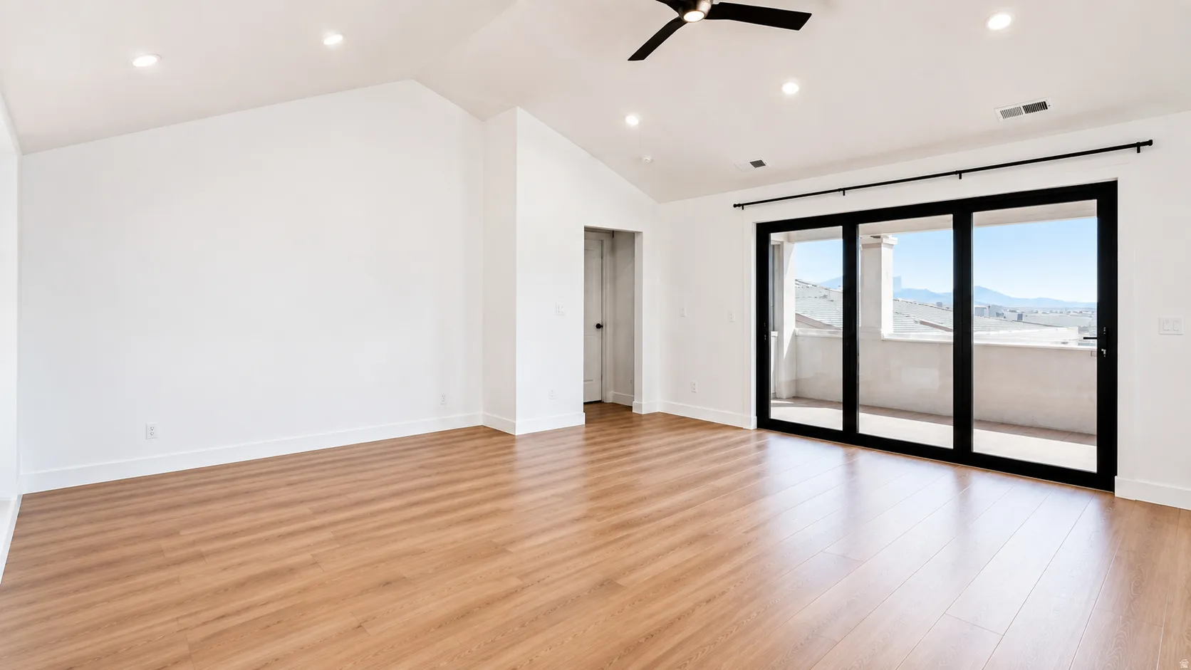 Expansive room with wood-finish flooring, vaulted ceiling, recessed lighting, and a contemporary ceiling fan