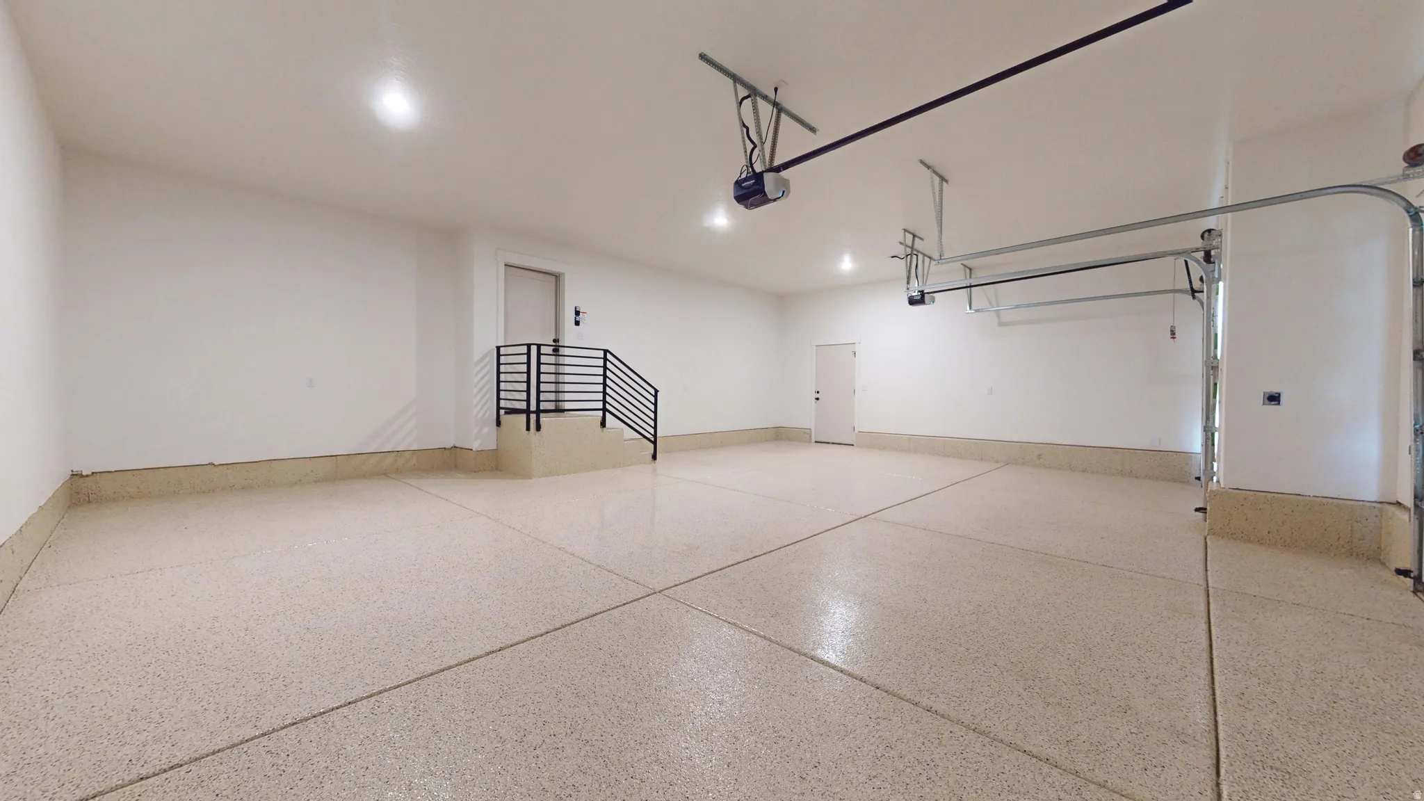 Spacious garage with epoxy flooring, recessed lighting, and a modern black metal staircase
