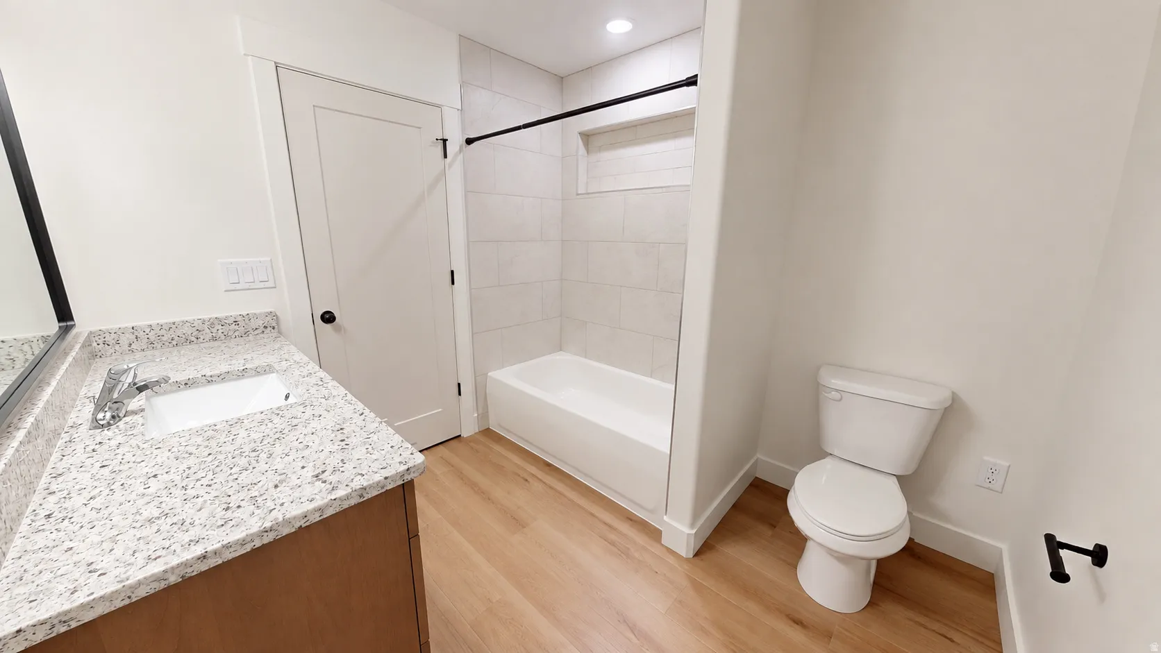 Bathroom featuring a wood-finish vanity with a light speckled countertop, an undermount sink, and a white bathtub with subway tile surround and a tiled niche