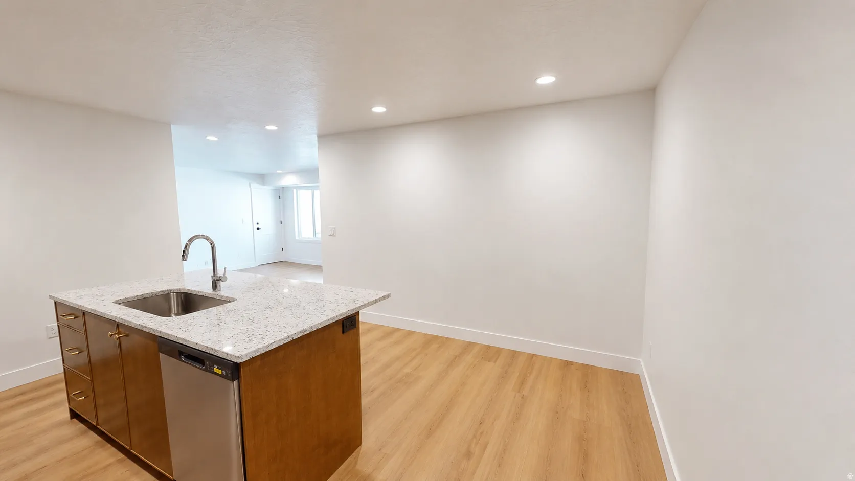 Kitchen island featuring a stainless steel sink with a high-arc faucet, integrated dishwasher, and light-toned countertop