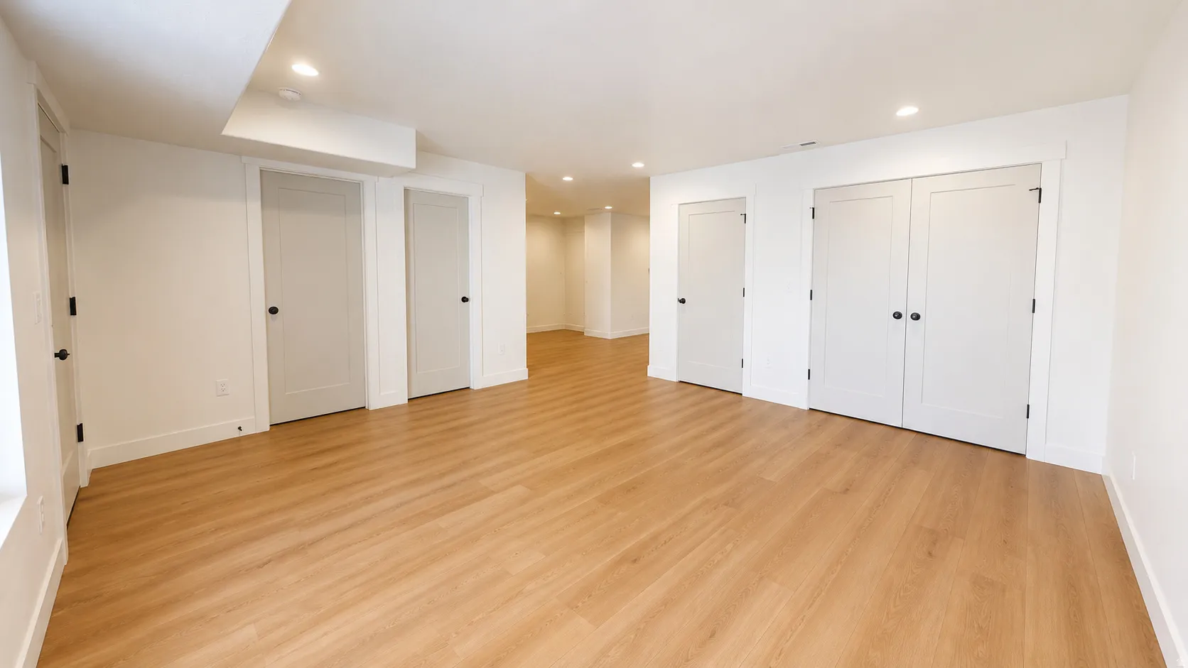 Expansive room featuring wood-finish flooring, recessed lighting, and multiple white panel doors with black hardware