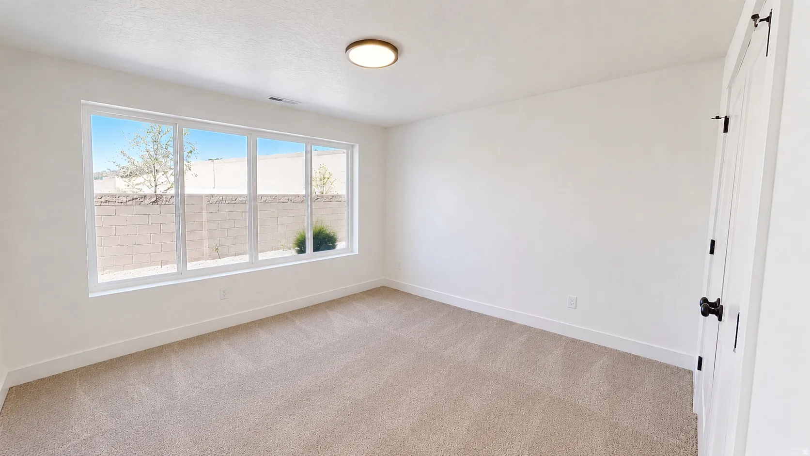 Expansive window providing ample natural light, neutral carpet flooring, recessed ceiling light fixture, white interior door with matte black hardware, and crisp white wall finishes