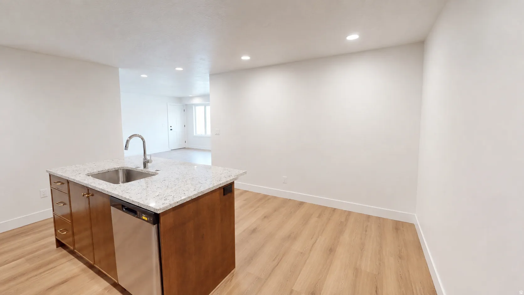 Kitchen island with a stainless steel sink, gooseneck faucet, integrated dishwasher, and light-toned countertop