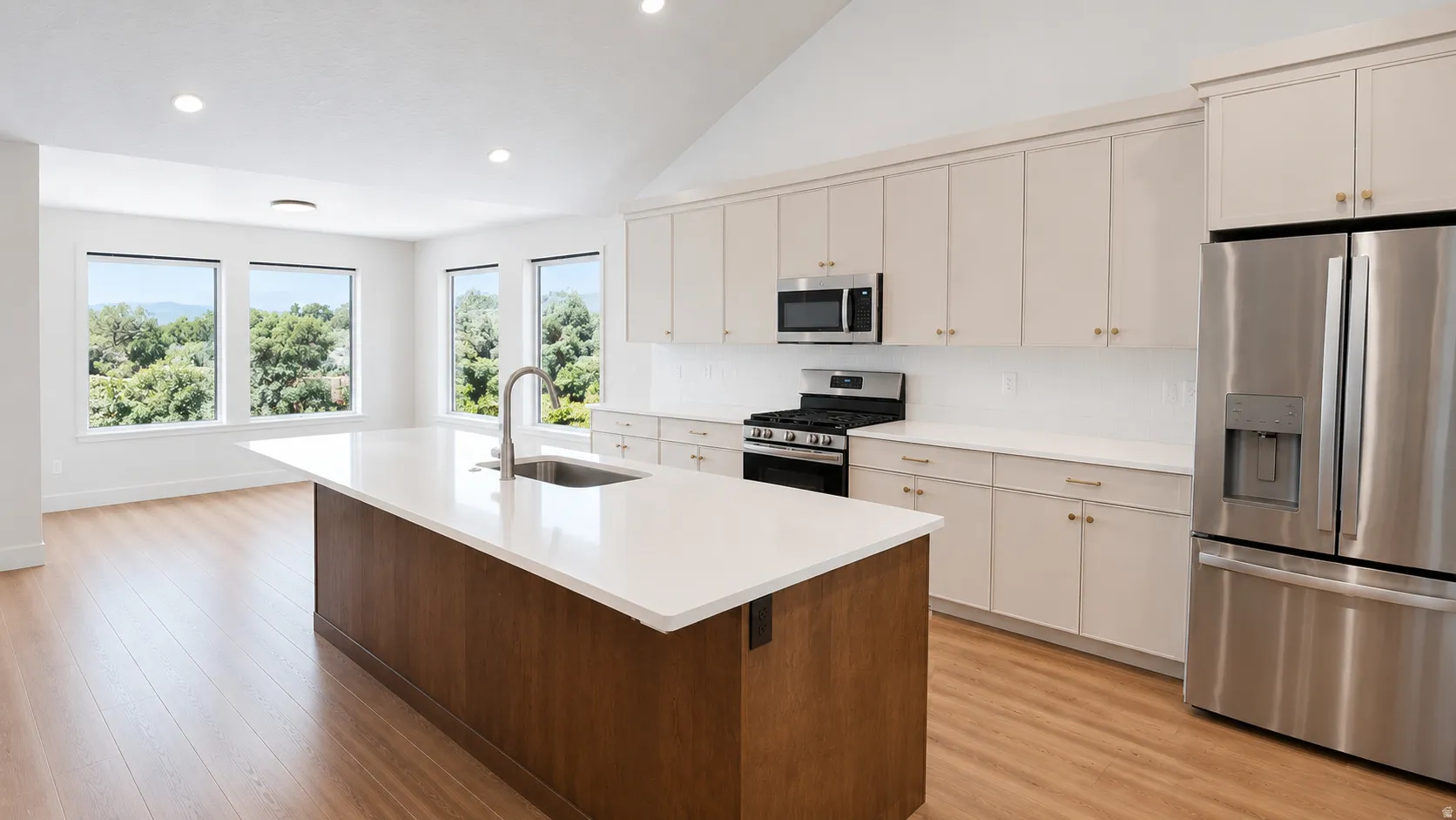 Well-appointed kitchen featuring a large central island with a sink, stainless steel appliances, light-toned cabinetry, and wood-finish flooring