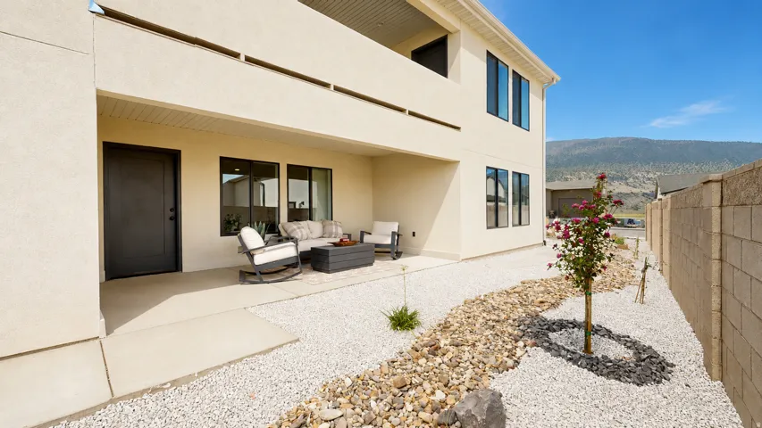 Rear patio with a concrete slab, upper-level balcony, xeriscape landscaping, and a privacy wall