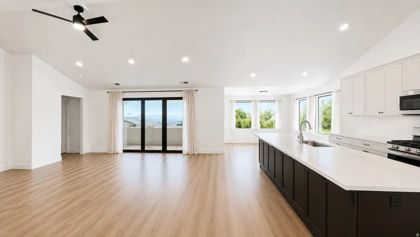 Vaulted ceilings with recessed lighting, wood-finish flooring, full kitchen with white cabinetry and dark island, stainless steel appliances, and glass doors to a balcony
