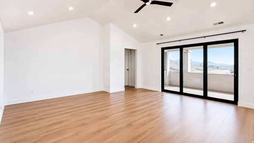 Expansive room with wood-finish flooring, vaulted ceiling, recessed lighting, and a contemporary ceiling fan