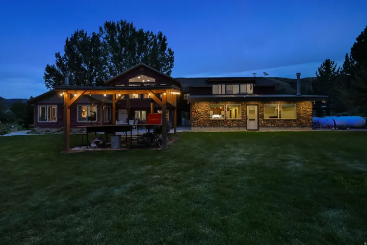 Stone-clad exterior, wood-sided addition, gabled roofline, expansive lawn, and outdoor pergola structure