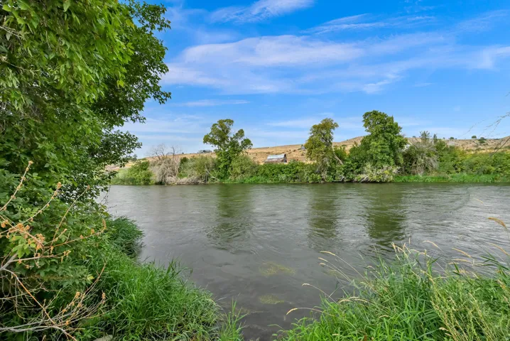 Riverfront property featuring a natural bank with lush vegetation and distant rolling hills