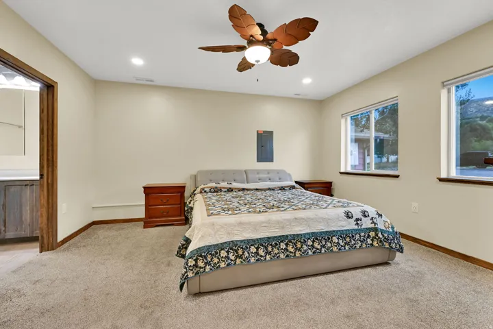 Recessed ceiling lighting, a ceiling fan with light, two windows, and a doorway with wood trim leading to a bathroom