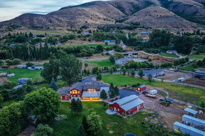 Expansive property featuring multiple structures, mature trees, manicured lawns, and a natural mountain backdrop