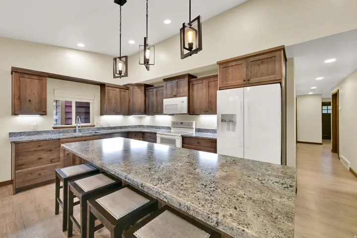 Kitchen featuring wood cabinetry, a center island with seating, a white refrigerator, and recessed and pendant lighting