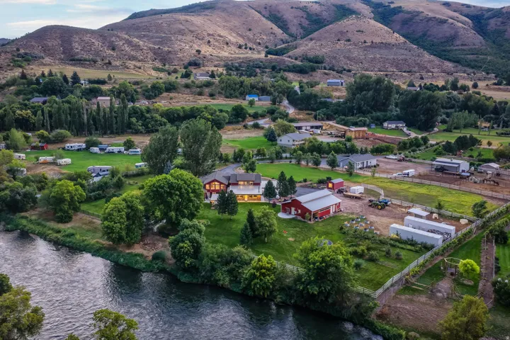 Expansive property with a river frontage, a two-story residence, a large red barn, and multiple outbuildings, all set against a mountainous backdrop
