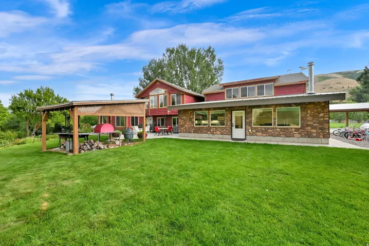 Expansive green lawn, stone exterior, red siding, covered patio, and large windows