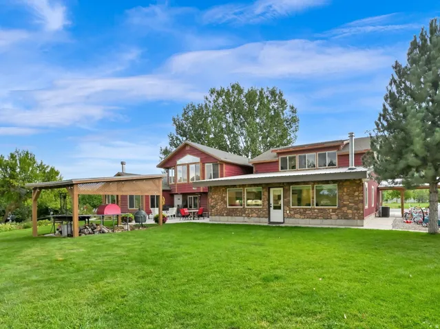 Expansive green lawn, red-sided residence with stone detailing, multiple windows, and a covered patio structure