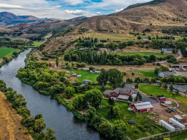 Riverfront property featuring a red-roofed residence, extensive green landscape, and surrounding mountainous terrain