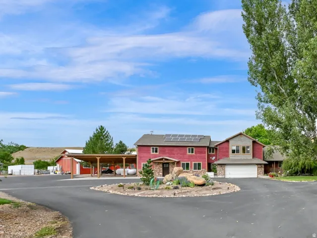 Paved circular driveway, attached garage, detached carport, solar panel installation, and mature landscaping