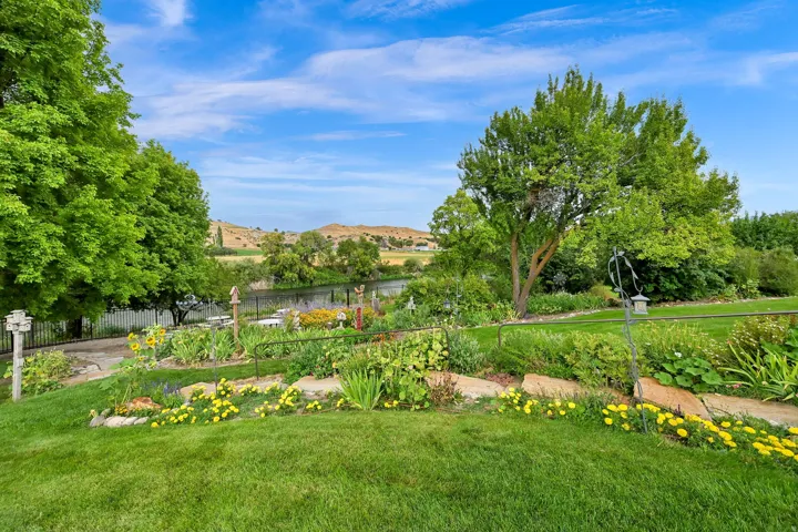 Expansive green lawn with established garden beds, mature trees, and a river backdrop