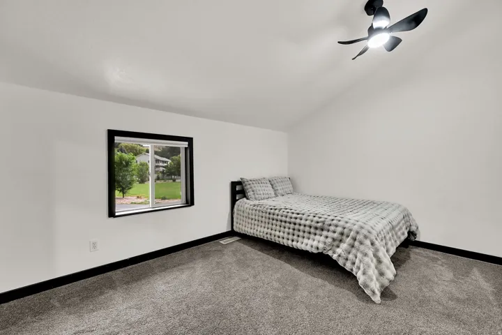 Vaulted ceiling room featuring a ceiling fan with integrated lighting, a sliding window with dark trim, and gray carpeting