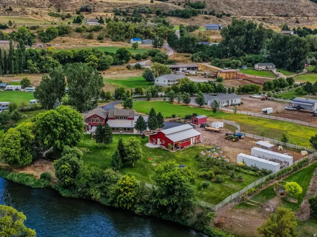 Riverfront property with multiple residential structures, agricultural buildings, and mountain scenery