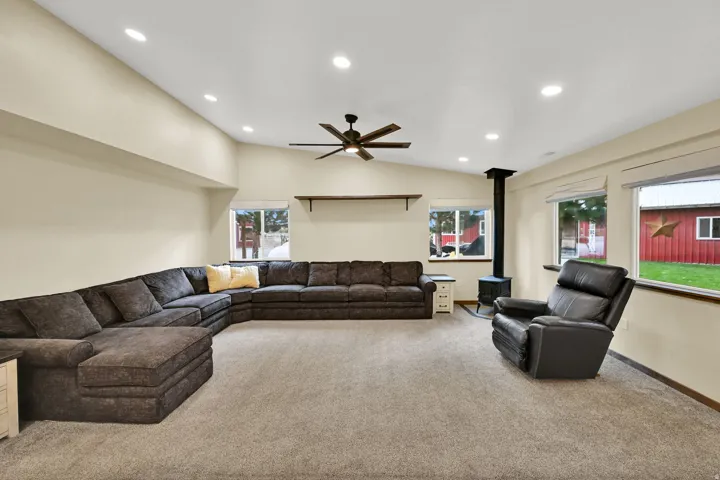 Vaulted ceiling with recessed lighting, exposed ceiling fan, built-in shelving, wood-burning stove, and multiple windows