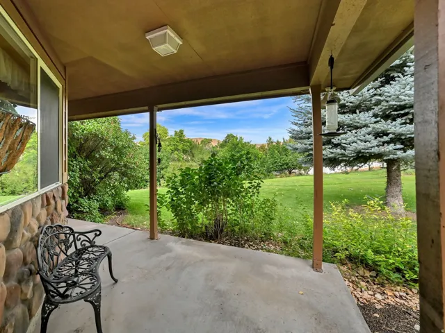 Covered concrete patio with a stone facade, wood siding, and mature landscaping