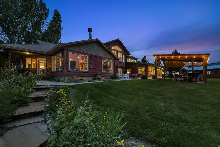 Expansive green lawn, stone-paved pathway, large windows, wood siding, and a spacious pergola with string lighting