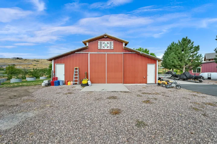 Red barn structure with corrugated metal siding, large sliding barn doors, two pedestrian access doors, and a gravel foreground