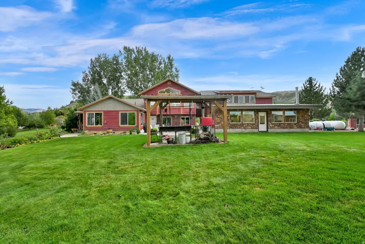 Expansive green lawn with mature trees and a multi-level structure featuring red siding and stone accents