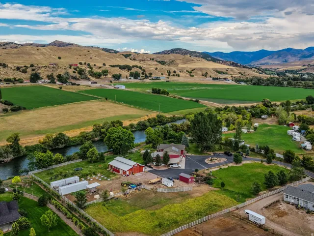 Expansive property featuring a river, mature trees, green fields, and distant mountains