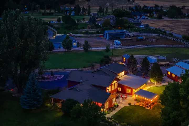 Stunning twilight aerial showcasing a contemporary residence with expansive illuminated outdoor living spaces, mature landscaping with specimen trees, manicured lawn grounds, and modern architectural design