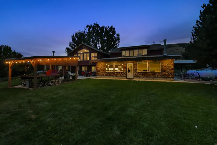 Expansive rear exterior featuring a stone facade, multiple windows, a rear entry door, and a covered patio structure