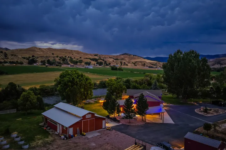 Expansive property featuring a main residence, an additional red barn structure, a paved circular driveway, mature trees, and a river