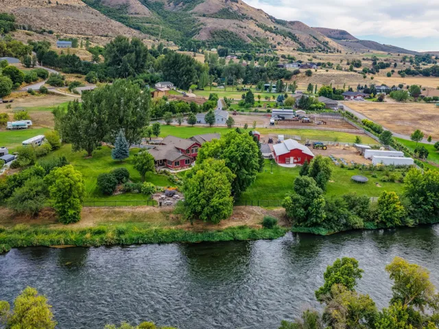 Expansive property featuring a waterfront setting, multiple structures, established landscaping, mountainous backdrop, and a river