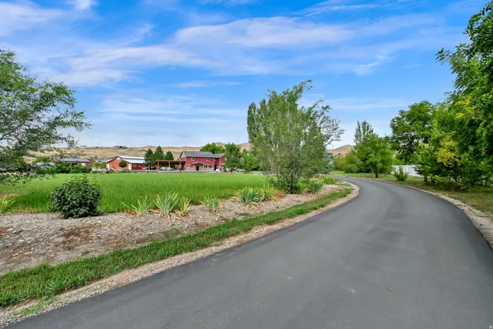 Paved drive, expansive green space, mature trees, red-painted exterior, covered patio