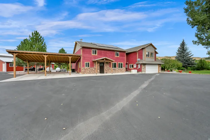 Red siding exterior with stone accents, attached two-car garage, and a covered carport