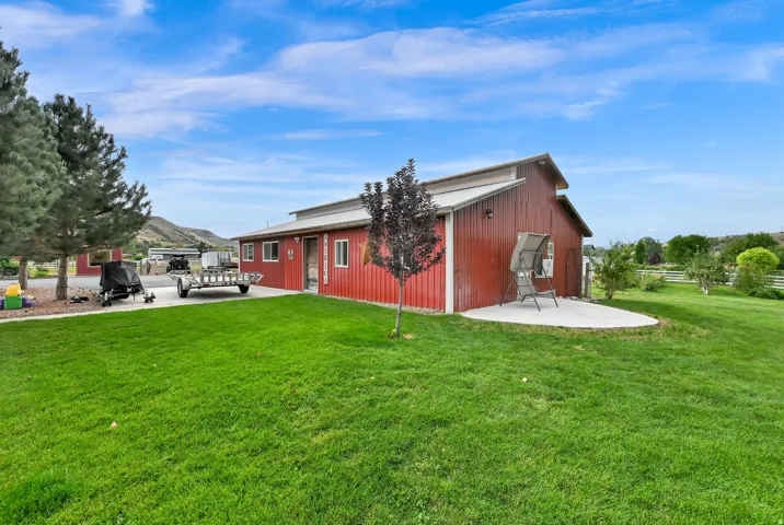 Expansive green lawn, red barn-style structure with white trim, mature trees, and a concrete patio