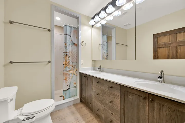 Dual vanity with integrated sinks, wood-finish cabinetry, chrome fixtures, and a spacious mirror