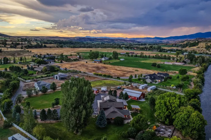 Expansive property featuring multiple structures, mature trees, open green spaces, and a river frontage