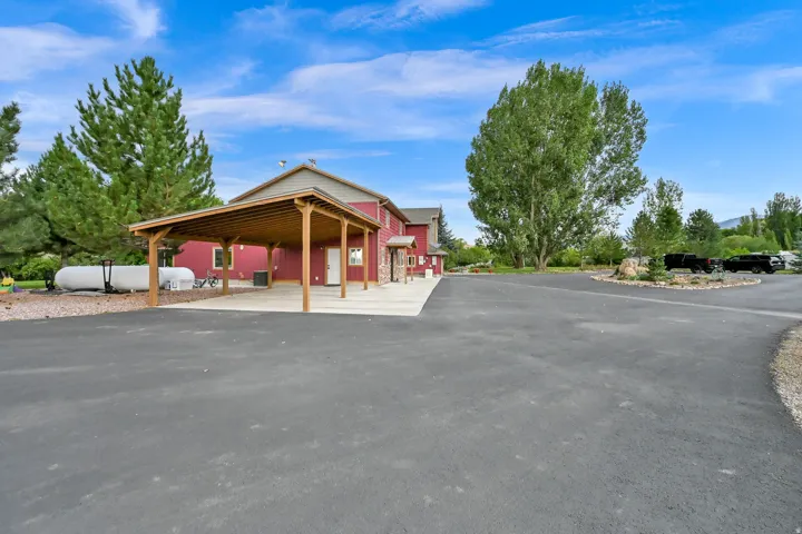 Expansive paved driveway leading to a covered carport, red siding, and stone accents