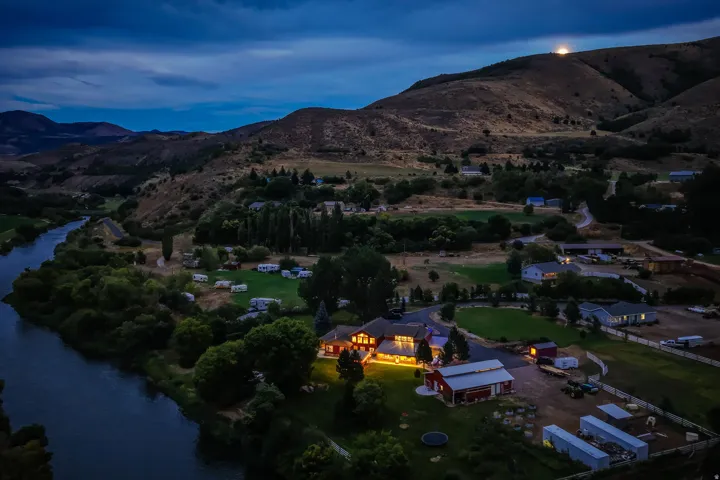Riverside property featuring expansive grounds, multiple structures including a main residence and outbuildings, and a mountainous backdrop