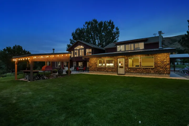 Stone facade, expansive lawn, covered patio, multiple large windows, attached carport