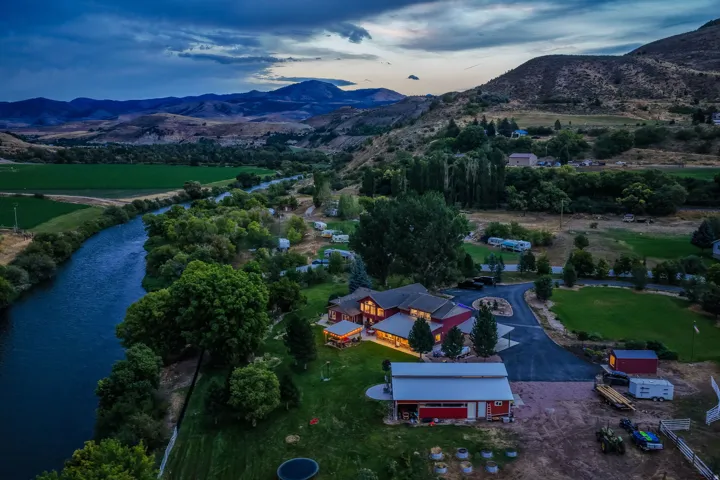 Expansive property featuring a riverfront setting, large red residence with multiple structures, paved driveway, and established landscaping