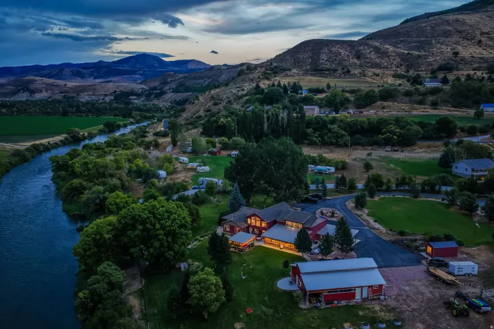 Expansive riverfront property with a primary residence, detached outbuilding, paved driveways, and surrounding mountainous terrain