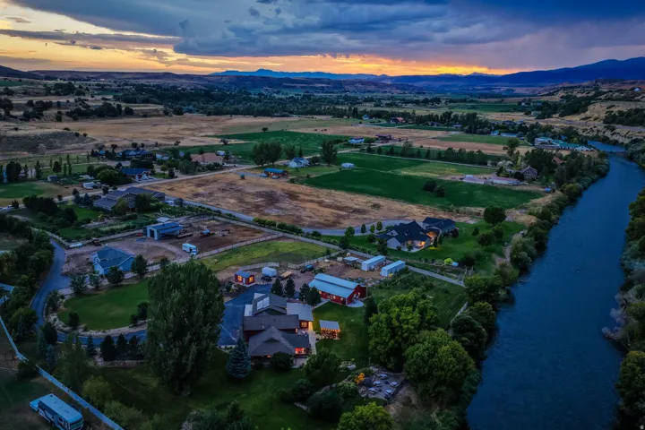 Expansive rural setting with a river, a large primary residence, multiple outbuildings, and surrounding agricultural land